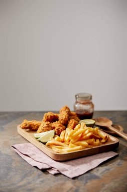 Lezzetli tavuk nugget, patates kızartması ve kireç içeren ahşap tahta, gri yüzeyde izole edilmiş.
