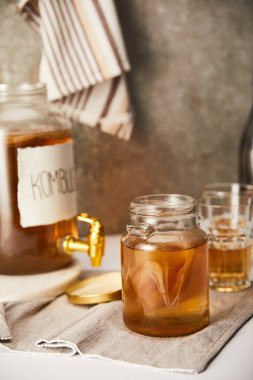 selective focus of jar with kombucha near glasses on textured grey background with striped napkin clipart