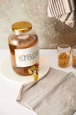 Kombuçalı kavanoz, çizgili peçeteli gri arka planda gözlüklerin yanında.