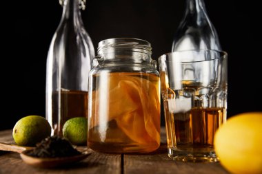 Kireç, limon, baharat ve şişe yanında kombu çayı olan cam kavanozun seçici odak noktası siyah masa üzerinde izole edilmiş ahşap masa.