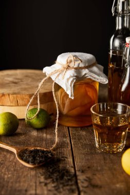 Limon, limon, baharat ve şişe yanında kombuçalı cam kavanoz siyah üzerine izole edilmiş ahşap masa.
