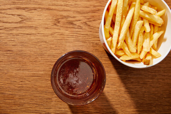 top view of beer in glass near delicious french fries in bucket on wooden background