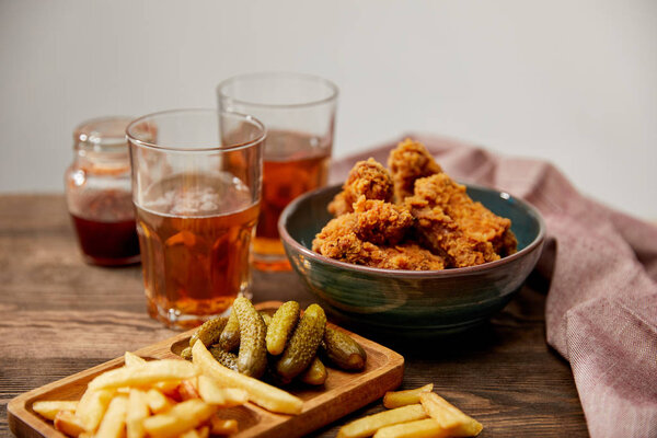 delicious chicken nuggets, french fries and gherkins near glasses of beer on wooden table isolated on grey