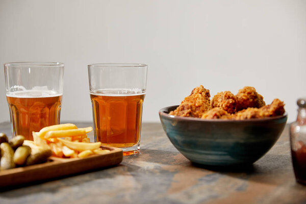 selective focus of delicious chicken nuggets, french fries and gherkins near glasses of beer on stone surface isolated on grey