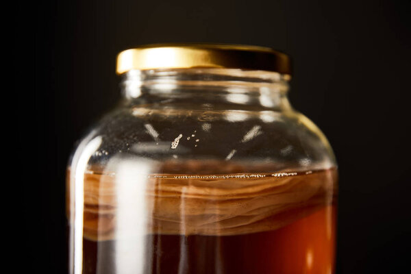 close up view of glass jar with kombucha isolated on black