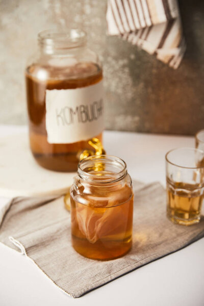 selective focus of jar with kombucha near glasses on textured grey background with striped napkin