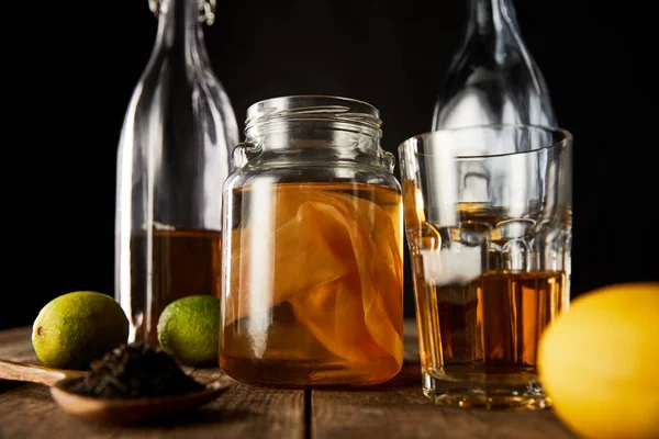 Kireç, limon, baharat ve şişe yanında kombu çayı olan cam kavanozun seçici odak noktası siyah masa üzerinde izole edilmiş ahşap masa.