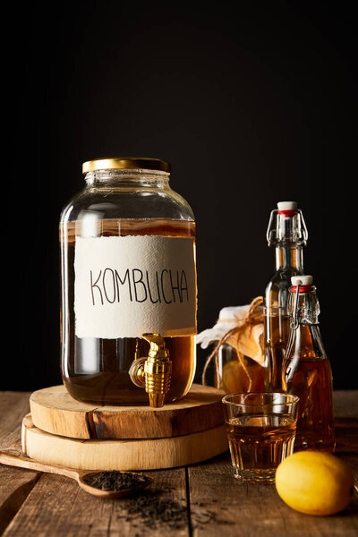 glass jar with kombucha near lemon, spice and bottles on wooden table isolated on black
