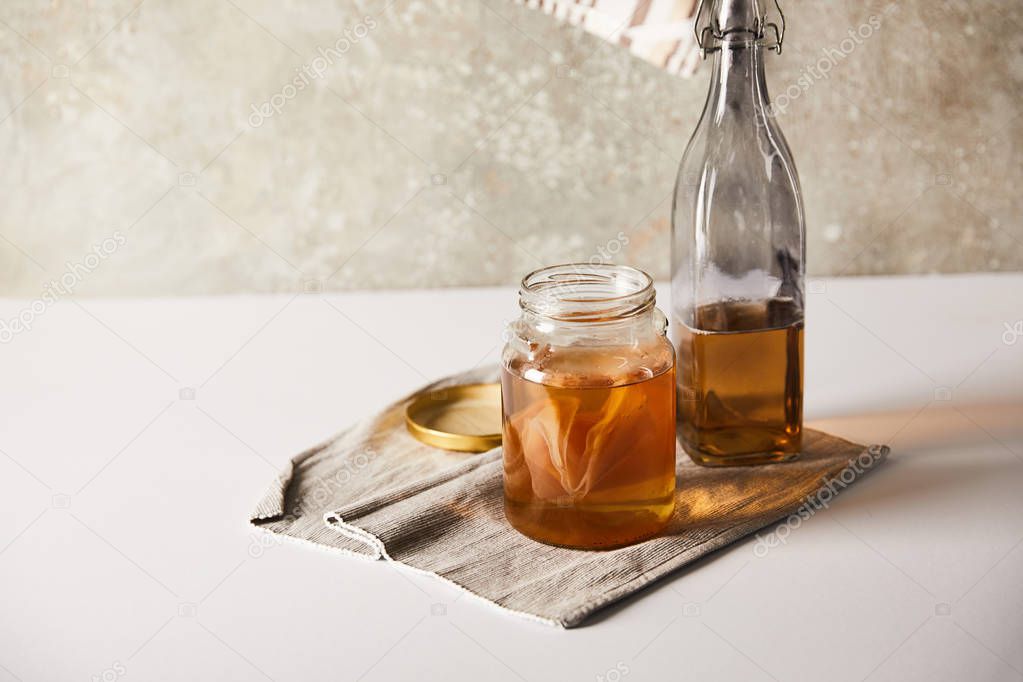 jar with kombucha near bottle on grey napkin on white table