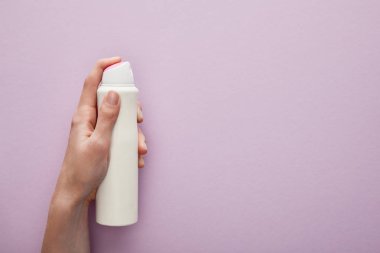 Menekşe arka planında sprey deodorant tutan beyaz güllü bir kadın görüntüsü.