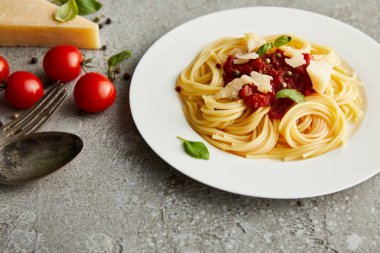 tasty bolognese pasta with tomato sauce and Parmesan on white plate near ingredients and cutlery on grey background clipart
