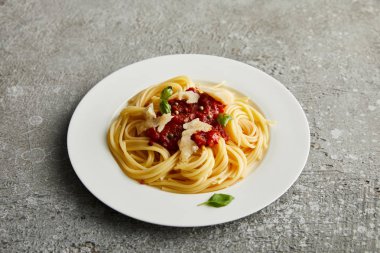 Domates soslu leziz bolonez makarna ve gri arka planda beyaz tabakta parmesan.