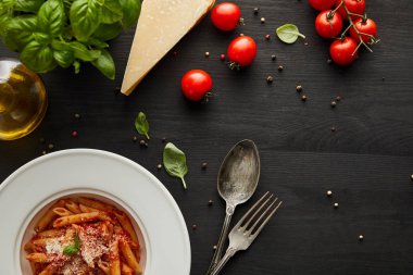 Domates soslu leziz bolonez makarna ve malzemelerin yanında beyaz tabakta parmesan ve siyah ahşap arka planda çatal bıçak seti.