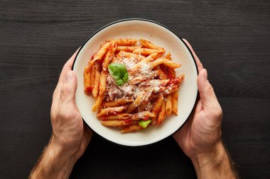 Adamın elinde domates soslu leziz bolonez makarnası ve siyah ahşap kaplama parmesan peyniri.