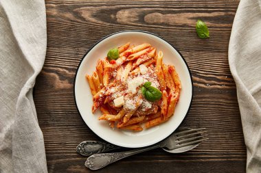 top view of tasty bolognese pasta with tomato sauce and Parmesan in white plate near cutlery on wooden background clipart