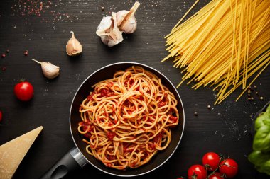 top view of tasty bolognese pasta in frying pan near ingredients on black wooden background clipart