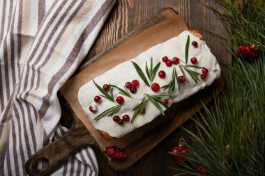 Geleneksel Noel pastasının en üst görüntüsü kırmızı takılar ve ahşap masa peçeteli çam ağacının yanındaki kızılcık dalının yanında.