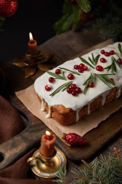 Çam ağacının yanında kızılcıklı geleneksel Noel pastası ve ahşap masada mumlar.
