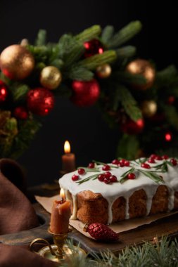 Geleneksel Noel pastasının seçici odağı. Noel çelengi yanında. Mücevherler ve siyah üzerine izole edilmiş ahşap masada yanan mumlar.