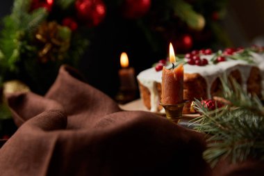 Geleneksel Noel pastasının seçici odağı, ahşap masada yanan mumların yanında kızılcık.