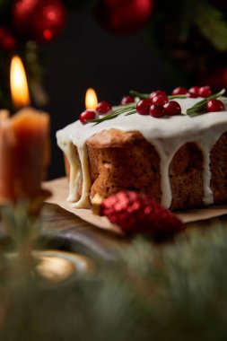 Geleneksel Noel pastasının seçici odağı, ahşap masada yanan mumların yanında kızılcık.