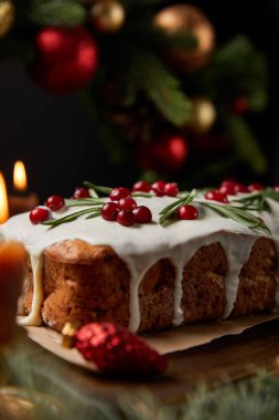 Geleneksel Noel pastasının seçici odağı, yanan mumların yanında kızılcık, ahşap masa üzerinde takılar olan Noel çelengi.