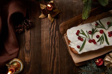 Geleneksel Noel pastasının üst görüntüsü, çam ağacının yanında, mücevherler ve ahşap masa üzerindeki mumlarla.