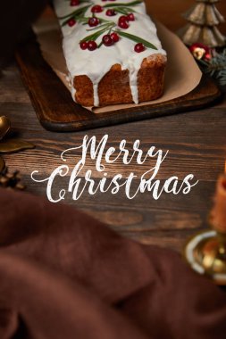 Kahverengi peçeteli ve beyaz mutlu noel harfleriyle ahşap masada kızılcıklı geleneksel Noel pastası.