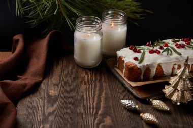 Geleneksel Noel pastası, mumların yanında kızılcık, peçete, mücevher ve ahşap masa üzerinde çam.