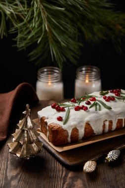 Çam ağacının yanında kızılcıklı geleneksel Noel pastası, ahşap masada mücevherler ve mumlar.