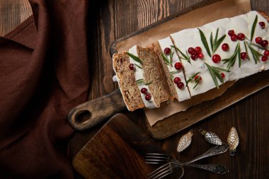 Geleneksel Noel pastasının en üst görüntüsü. Mücevherler, çatallar ve ahşap masanın üzerindeki kahverengi peçeteler yanında kızılcık var.