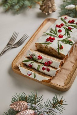 traditional Christmas cake with cranberry near forks, baubles and pine on white table