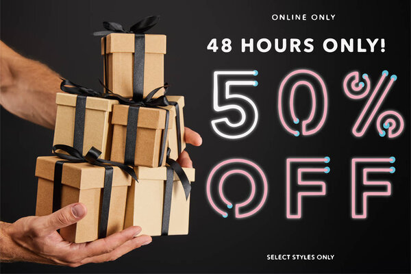 cropped view of man holding cardboard gift boxes with ribbons isolated on black with 48 hours 50 percent off illustration, black Friday concept