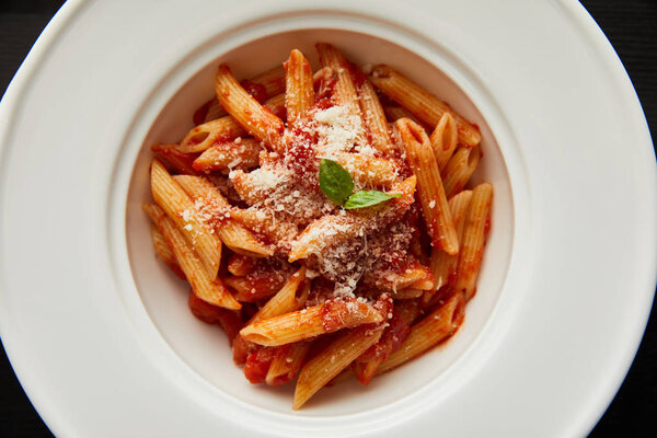 top view of tasty bolognese pasta with tomato sauce and Parmesan in white plate isolated on black