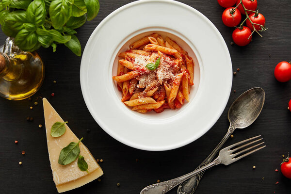 top view of tasty bolognese pasta with tomato sauce and Parmesan in white plate near ingredients and cutlery on black wooden background