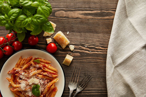 top view of tasty bolognese pasta with tomato sauce and Parmesan in white plate near ingredients and cutlery on wooden table