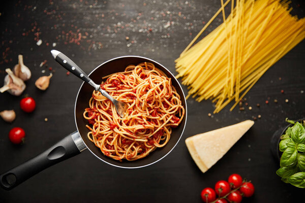 селективный фокус вкусной пасты болоньезе в сковороде вблизи ингредиентов на черном деревянном фоне
