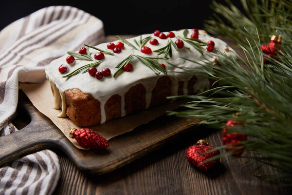 традиционный рождественский торт с клюквой возле сосновой ветки с красными безделушками и салфеткой на деревянном столе, изолированном на черном
