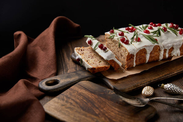 traditional Christmas cake with cranberry near baubles, fork and brown napkin on wooden table isolated on black