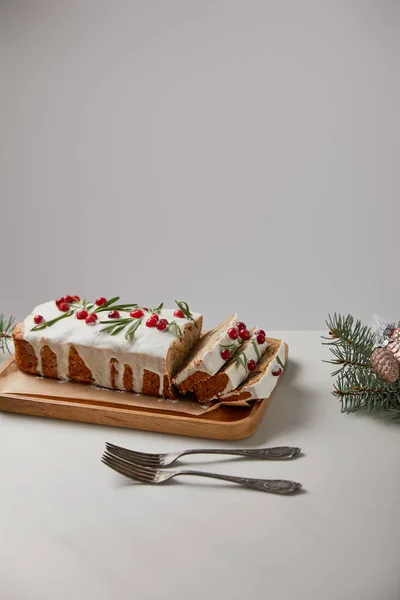 traditional Christmas cake with cranberry near forks, baubles and pine on white table isolated on grey