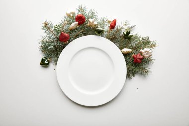 Beyaz arka planda mücevherleri olan Noel ağacı dalının yanındaki beyaz tabağın üst görüntüsü
