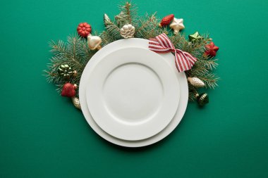 Yeşil arka planda mücevherleri olan Noel ağacı dalının yanındaki beyaz tabakaların üst görüntüsü