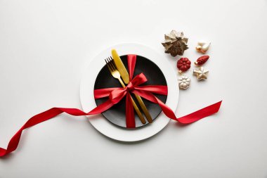 Beyaz ve siyah tabakların üst görünümü çatal bıçak ve kurdele ile beyaz arka planda neşeli Noel mücevherleri