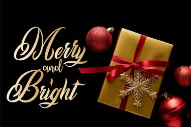 Kırmızı kurdeleli ve mücevherlerin yakınındaki kar taneli parlak altın Noel hediyesinin en üst görüntüsü. Siyah üzerine izole edilmiş, neşeli ve parlak bir resimle.