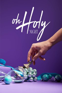 cropped view of woman touching Christmas decoration and hourglass scattered on purple background with o holy night illustration clipart