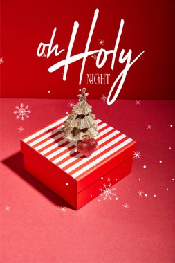 Çizgili kırmızı hediye kutusu ve süslemeli altın Noel ağacı. Kırmızı arka planda, o kutsal gece illüstrasyonuyla.