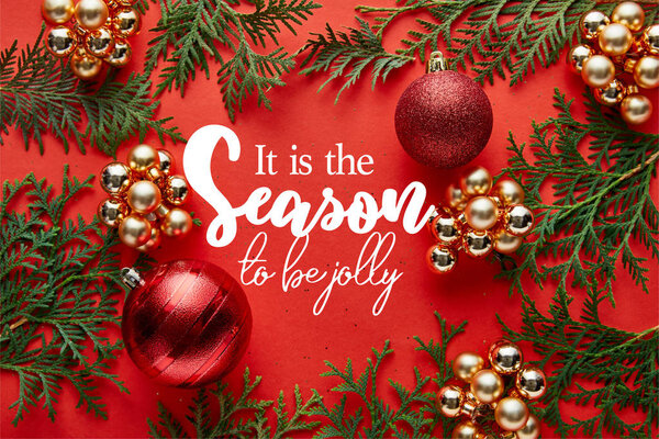 Top view of shiny Christmas decoration and thuja on red background with it is the season to be jolly lettering
