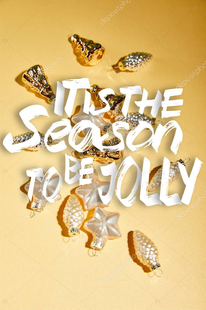 golden Christmas baubles on yellow background with it is the season to be jolly lettering