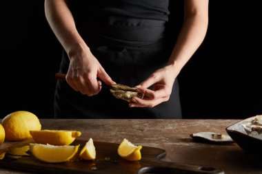 Kesme tahtasındaki limonların yanında istiridye açarken bıçak tutan kadın görüntüsü. 
