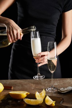 Seçici odak noktası, şampanya bardağına köpüklü şarap döken istiridye ve siyah üzerine izole edilmiş limonlar. 